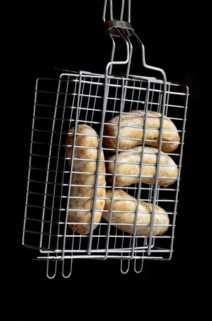 A small hand grill is filled with fried thick sausages on a dark backgroundの写真素材