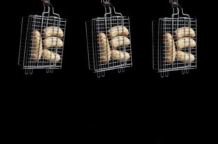 A small hand grill is filled with fried thick sausages on a dark backgroundの写真素材