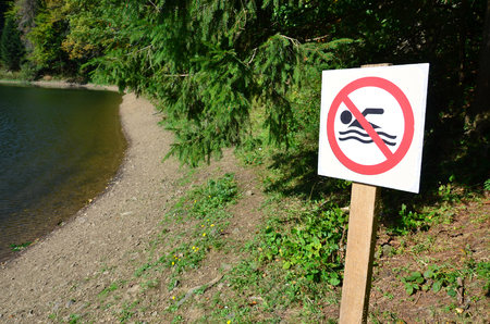 A pillar with a sign denoting a ban on swimming. The sign shows a crossed-out floating personの写真素材