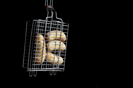 A small hand grill is filled with fried thick sausages on a dark backgroundの写真素材