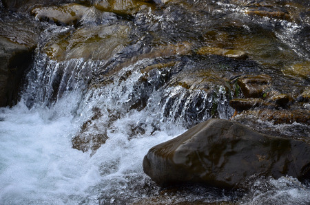 Close-up image of a small wild waterfall in the form of short streams of water between mountain stonesの写真素材