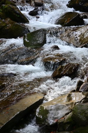 Close-up image of a small wild waterfall in the form of short streams of water between mountain stonesの写真素材