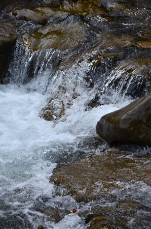 Close-up image of a small wild waterfall in the form of short streams of water between mountain stonesの写真素材