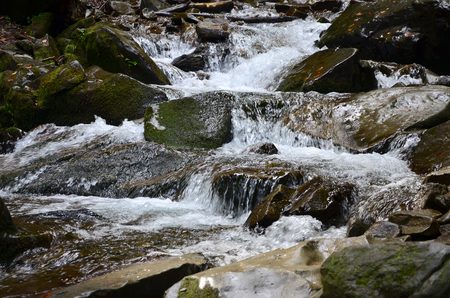 Close-up image of a small wild waterfall in the form of short streams of water between mountain stonesの写真素材