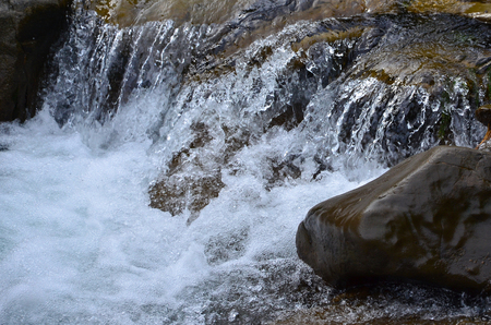 Close-up image of a small wild waterfall in the form of short streams of water between mountain stonesの写真素材