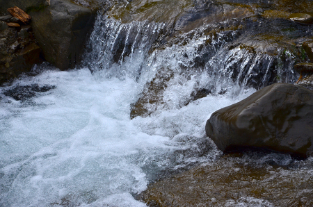 Close-up image of a small wild waterfall in the form of short streams of water between mountain stonesの写真素材