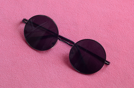Stylish black sunglasses with round glasses lies on a blanket made of soft and fluffy light pink fleece fabric. Fashionable background picture in female colorsの写真素材