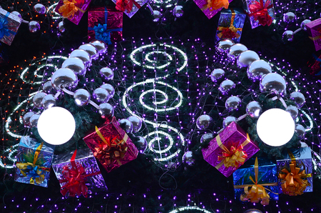 A fragment of a huge Christmas tree with many ornaments, gift boxes and luminous lamps. Photo of a decorated Christmas tree close-upの写真素材