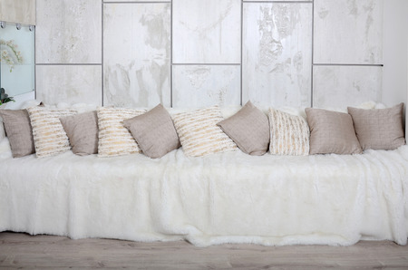 Many pillows lie on the couch, which is covered with a large plush veil against the background of a marble wallの写真素材