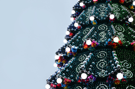 A fragment of a huge Christmas tree with many ornaments, gift boxes and luminous lamps. Photo of a decorated Christmas tree close-up with copy spaceの写真素材