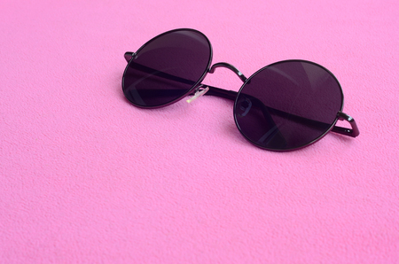 Stylish black sunglasses with round glasses lies on a blanket made of soft and fluffy light pink fleece fabric. Fashionable background picture in female colorsの写真素材