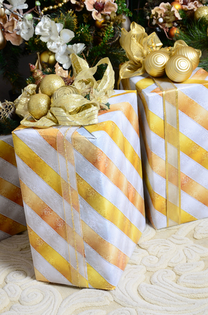 Photo of luxury gift boxes under Christmas tree, New Year home decorations, golden wrapping of Santa presents, festive fir tree decorated with garland, baubles and toys, traditional celebrationの写真素材