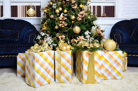 Photo of luxury gift boxes under Christmas tree, New Year home decorations, golden wrapping of Santa presents, festive fir tree decorated with garland, baubles and toys, traditional celebrationの写真素材