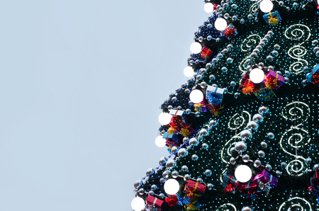 A fragment of a huge Christmas tree with many ornaments, gift boxes and luminous lamps. Photo of a decorated Christmas tree close-up with copy spaceの写真素材