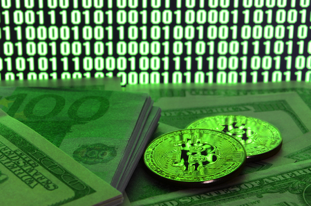 Two bitcoins lies on a pile of dollar bills on the background of a monitor depicting a binary code of bright green zeros and one units on a black background. Low key lightingの写真素材