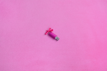 Brilliant pink usb flash memory card with a pink bow lies on a blanket of soft and furry light pink fleece fabric. Classic female gift design for a memory cardの写真素材