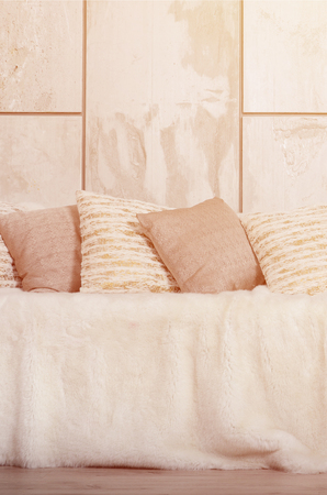 Many pillows lie on the couch, which is covered with a large plush veil against the background of a marble wallの写真素材