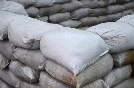 Background of many dirty sand bags for flood defense. Protective sandbag barricade for military use. Handsome tactical bunkerの写真素材