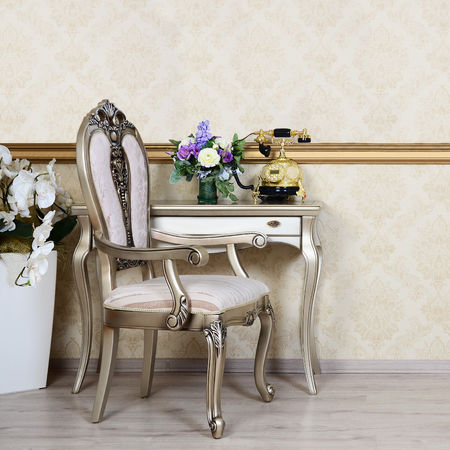 A fragment of a retro interior with a chair and a desk on which is located a telephone and a vase of flowersの写真素材