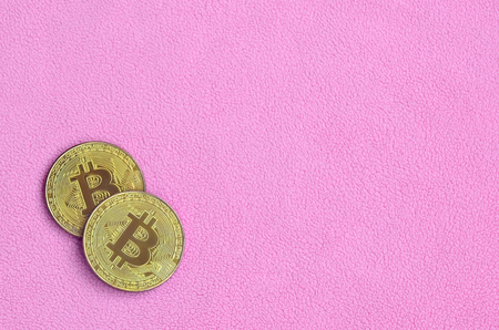 Two golden bitcoins lies on a blanket made of soft and fluffy light pink fleece fabric. Physical visualization of virtual crypto currencyの写真素材