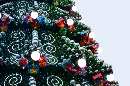 A fragment of a huge Christmas tree with many ornaments, gift boxes and luminous lamps. Photo of a decorated Christmas tree close-up with copy spaceの写真素材