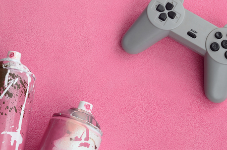 Teenagers and youth lifestyle concept. Joystick and two spray cans lies on the blanket of furry pink fleece fabric. Controllers for video games and paint cans on a plush fleece material backgroundの写真素材