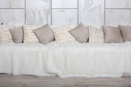 Many pillows lie on the couch, which is covered with a large plush veil against the background of a marble wallの写真素材