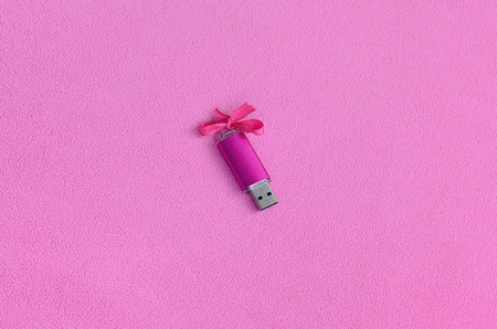 Brilliant pink usb flash memory card with a pink bow lies on a blanket of soft and furry light pink fleece fabric. Classic female gift design for a memory cardの写真素材