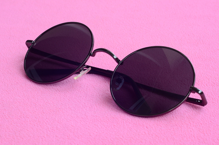 Stylish black sunglasses with round glasses lies on a blanket made of soft and fluffy light pink fleece fabric. Fashionable background picture in female colorsの写真素材