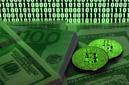 Two bitcoins lies on a pile of dollar bills on the background of a monitor depicting a binary code of bright green zeros and one units on a black background. Low key lightingの写真素材