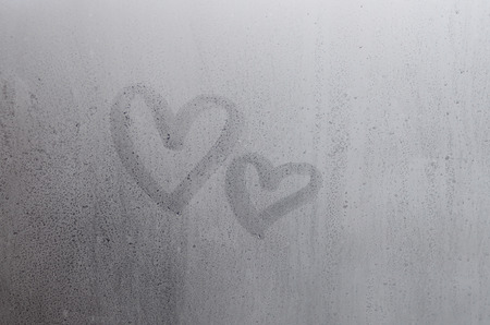 Couple of abstract blurred love heart symbol drawn by hand on the wet window glass with sunlight background. Template for Valentine Day postcardsの写真素材