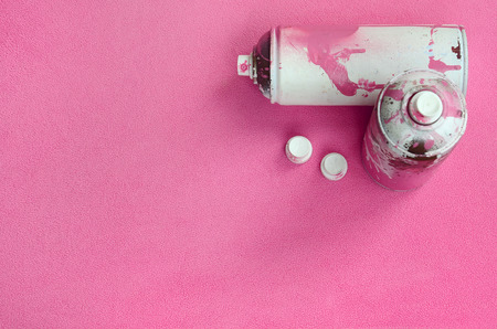 Some used pink aerosol spray cans and nozzles with paint drips lies on a blanket of soft and furry light pink fleece fabric. Classic female design color. Graffiti hooliganism conceptの写真素材