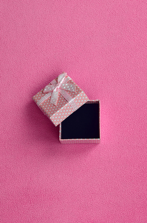 Open small gift box in pink with a small bow lies on a blanket of soft and furry light pink fleece fabric. Packing for a gift to your lovely girlfriendの写真素材