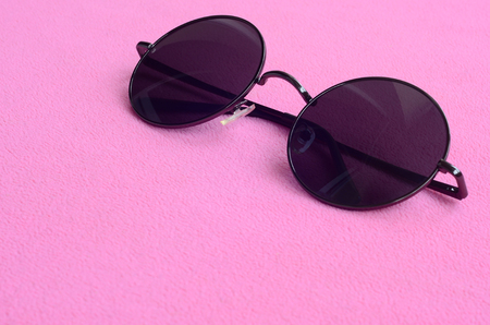 Stylish black sunglasses with round glasses lies on a blanket made of soft and fluffy light pink fleece fabric. Fashionable background picture in female colorsの写真素材