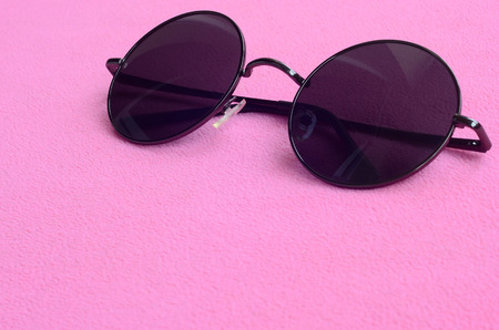 Stylish black sunglasses with round glasses lies on a blanket made of soft and fluffy light pink fleece fabric. Fashionable background picture in female colorsの写真素材