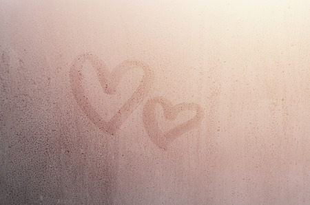 Couple of abstract blurred love heart symbol drawn by hand on the wet window glass with sunlight background. Template for Valentine Day postcardsの写真素材