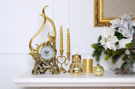 New Year and Christmas composition. Decorative golden clock, thick candles, candlestick, pot of flowers and framed canvas that hangs on the wallの写真素材