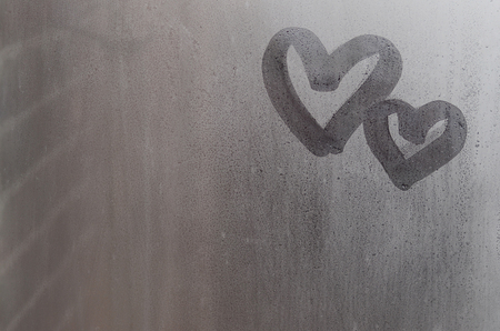 Couple of abstract blurred love heart symbol drawn by hand on the wet window glass with sunlight background. Template for Valentine Day postcardsの写真素材