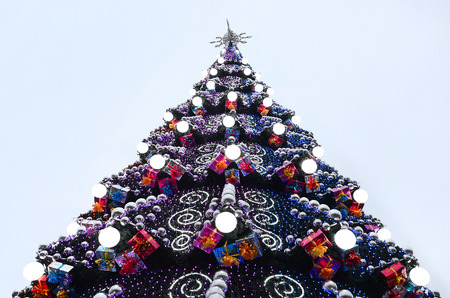 A fragment of a huge Christmas tree with many ornaments, gift boxes and luminous lamps. Photo of a decorated Christmas tree close-up with copy spaceの写真素材