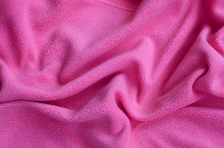 The blanket of furry pink fleece fabric. A background of light pink soft plush fleece material with a lot of relief foldsの写真素材