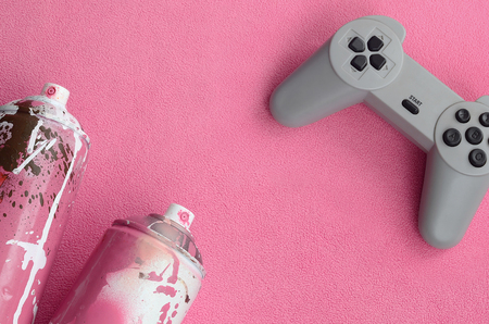 Teenagers and youth lifestyle concept. Joystick and two spray cans lies on the blanket of furry pink fleece fabric. Controllers for video games and paint cans on a plush fleece material backgroundの写真素材