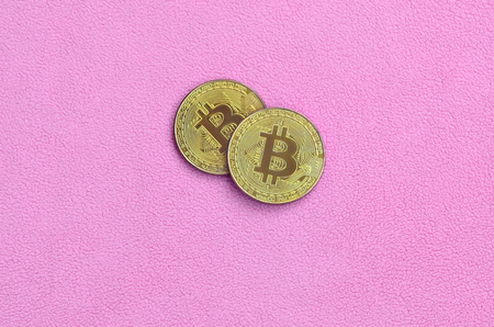 Two golden bitcoins lies on a blanket made of soft and fluffy light pink fleece fabric. Physical visualization of virtual crypto currencyの写真素材