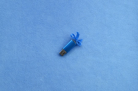 Brilliant blue usb flash memory card with a blue bow lies on a blanket of soft and furry light blue fleece fabric. Classic female gift design for a memory cardの写真素材