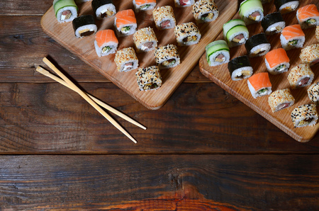 A detailed shot of a set of Japanese sushi rolls and a device for their use (chopsticks), which are located on a wooden cutting board on a table in the kitchen of a sushi barの写真素材