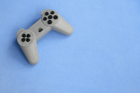 Playing games concept. Single pad joystick lies on the blanket of furry blue fleece fabric. Controller for video games on a background texture of light blue soft plush fleece materialの写真素材