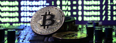 Two bitcoins lies on a videocard surface with background of screen display of cryptocurrency mining by using the GPUsの写真素材