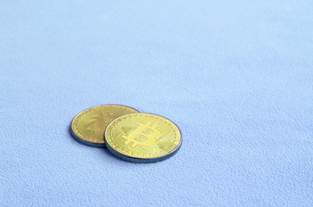 Two golden bitcoins lies on a blanket made of soft and fluffy light blue fleece fabric. Physical visualization of virtual crypto currencyの写真素材