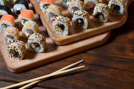 A detailed shot of a set of Japanese sushi rolls and a device for their use (chopsticks), which are located on a wooden cutting board on a table in the kitchen of a sushi barの写真素材