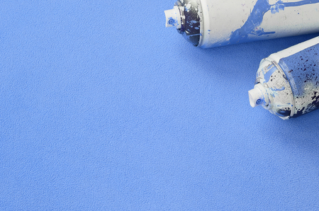 Some used blue aerosol spray cans with paint drips lies on a blanket of soft and furry light blue fleece fabric. Classic female design color. Graffiti hooliganism conceptの写真素材