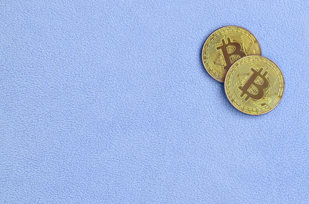 Two golden bitcoins lies on a blanket made of soft and fluffy light blue fleece fabric. Physical visualization of virtual crypto currencyの写真素材